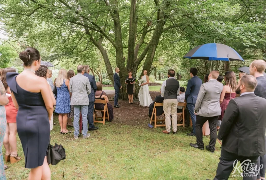 A wide shot down the aisle of a wedding ceremony under a big tree at Edwards Gardens