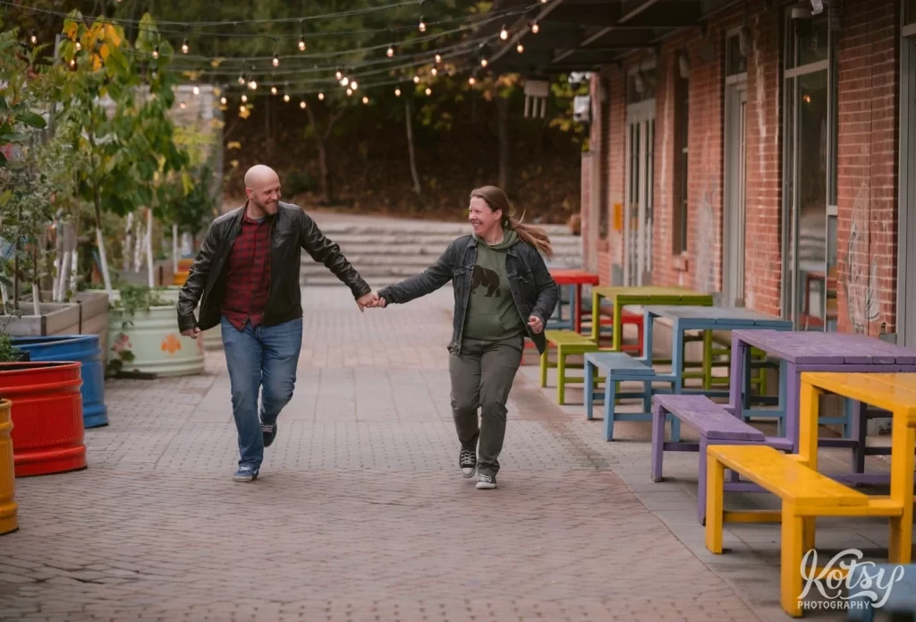 A couple are all laughs as they run towards the camera while holding hands at Evergreen Brick Works in Toronto