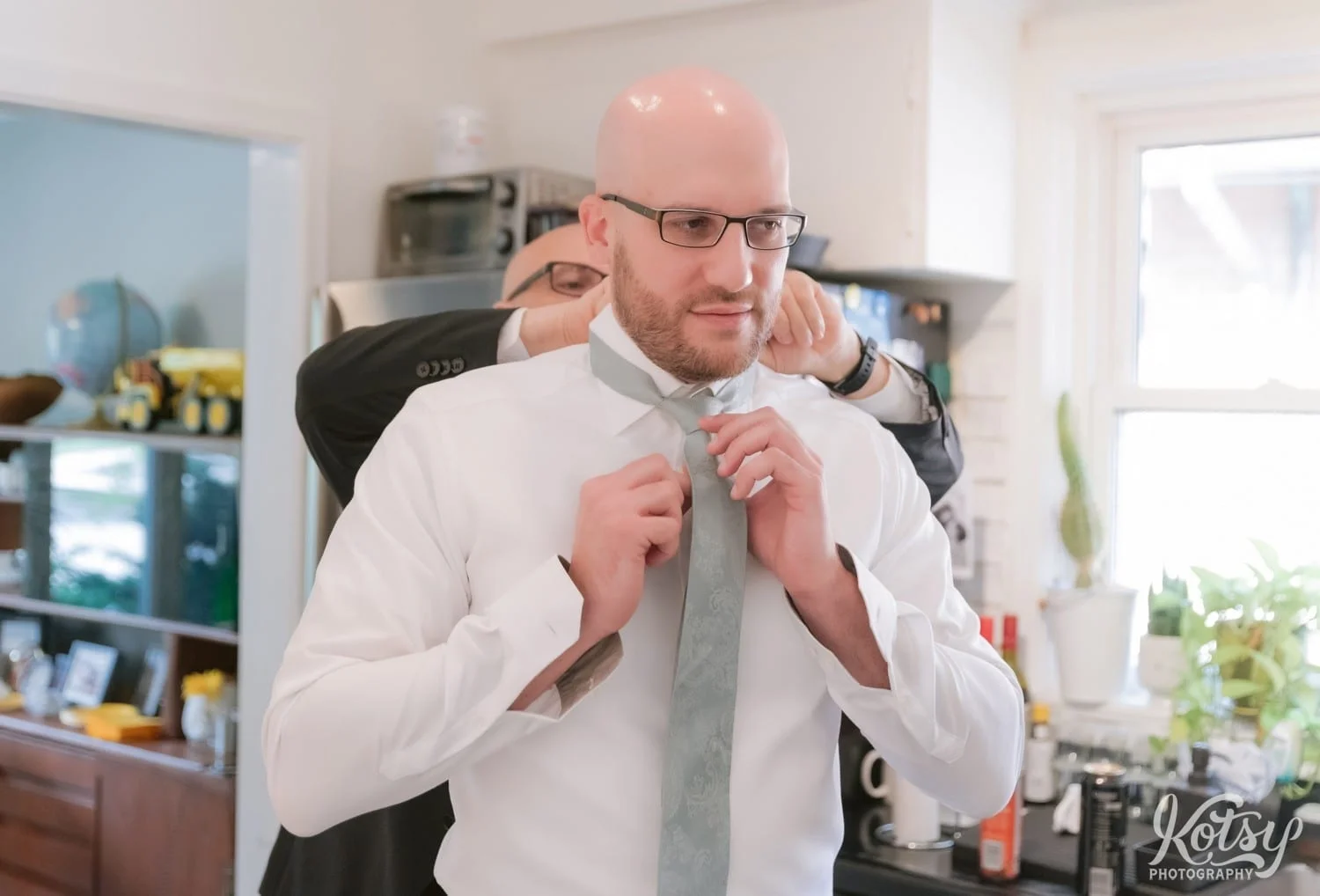 a groom does up his tie as a man adjusts his collar