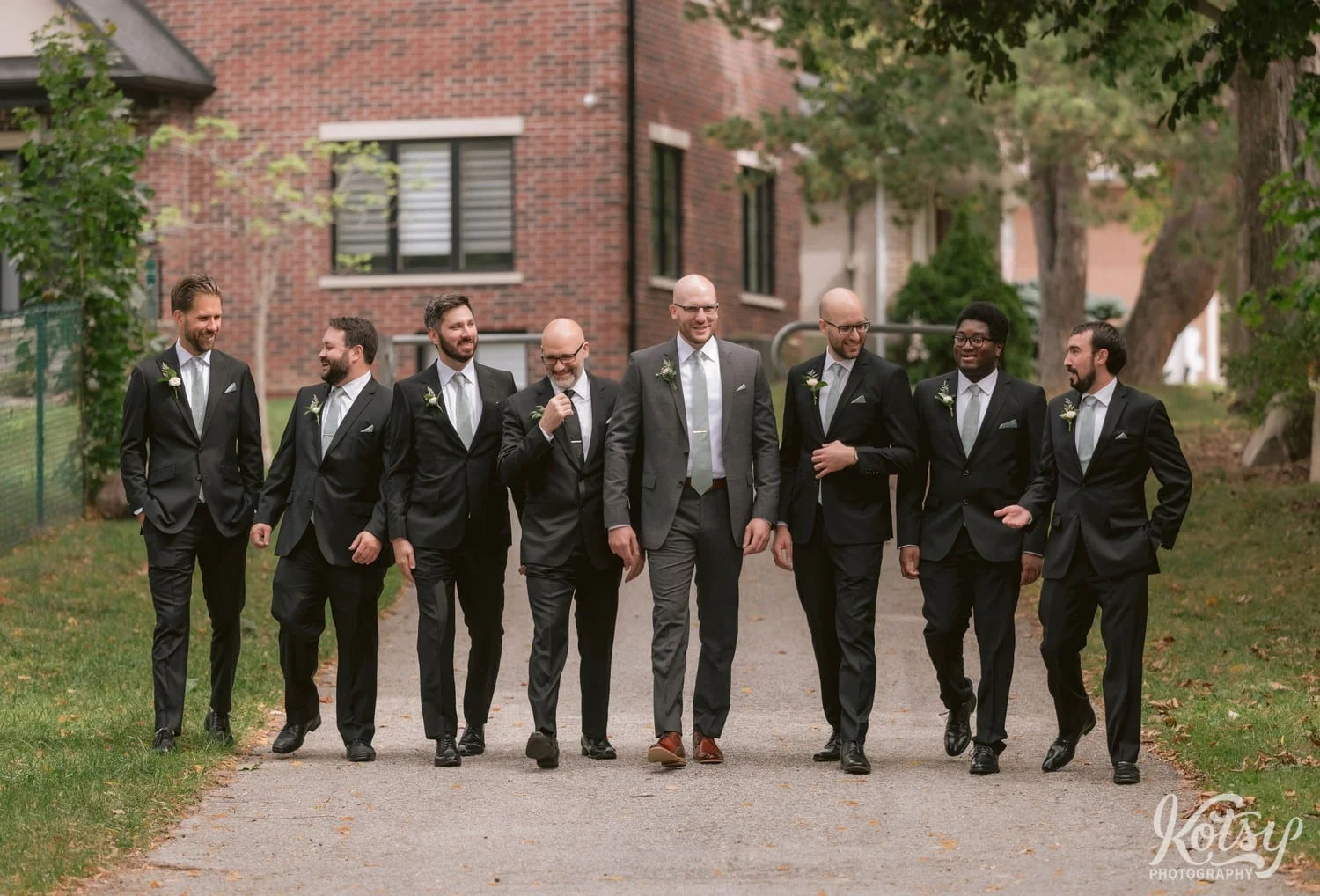 A group of groomsmen and groom walk towards the camera on a path at West Deane Park in Toronto, Canada