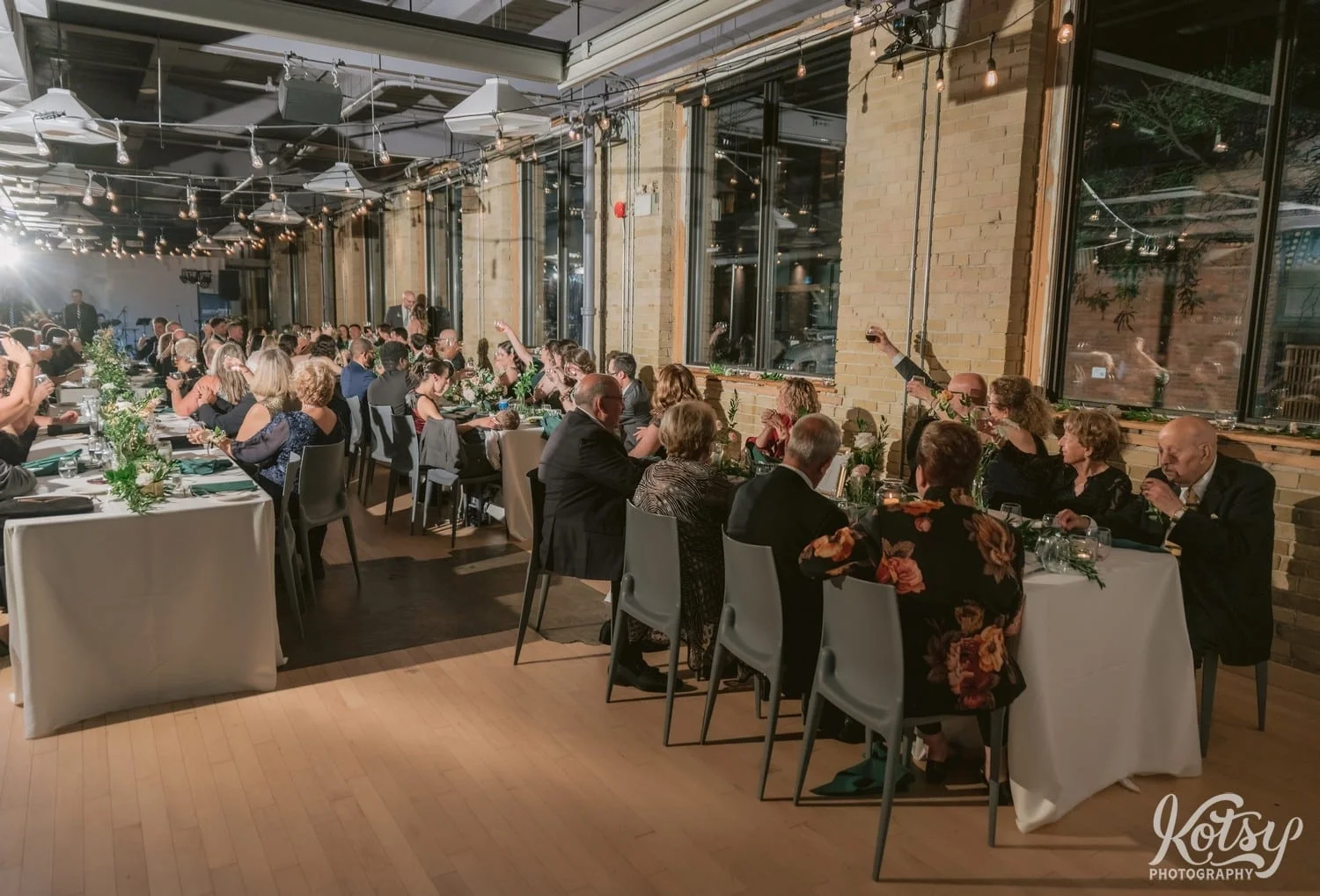 A room full of people sitting at tables raise their glass and cheers during a Second Floor Events wedding reception in Toronto, Canada.