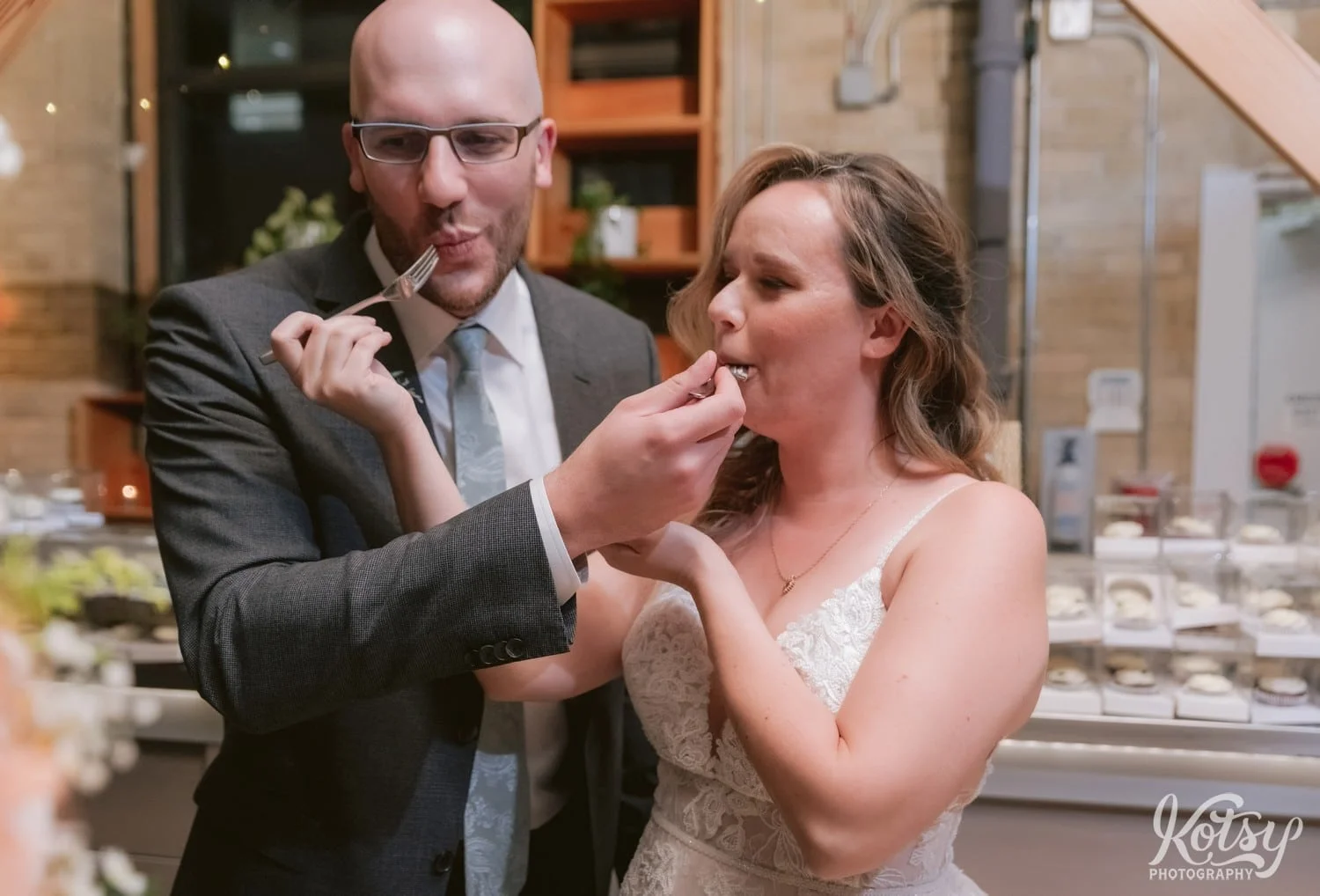 A bride in a white wedding gown and groom in gray suit feed each other a piece of cake during their Second Floor Events wedding reception in Toronto, Canada.