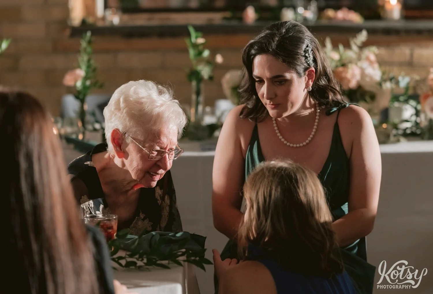 An elderly woman looks down to a woman crouch speaking to her during a Second Floor Events wedding reception in Toronto, Canada.