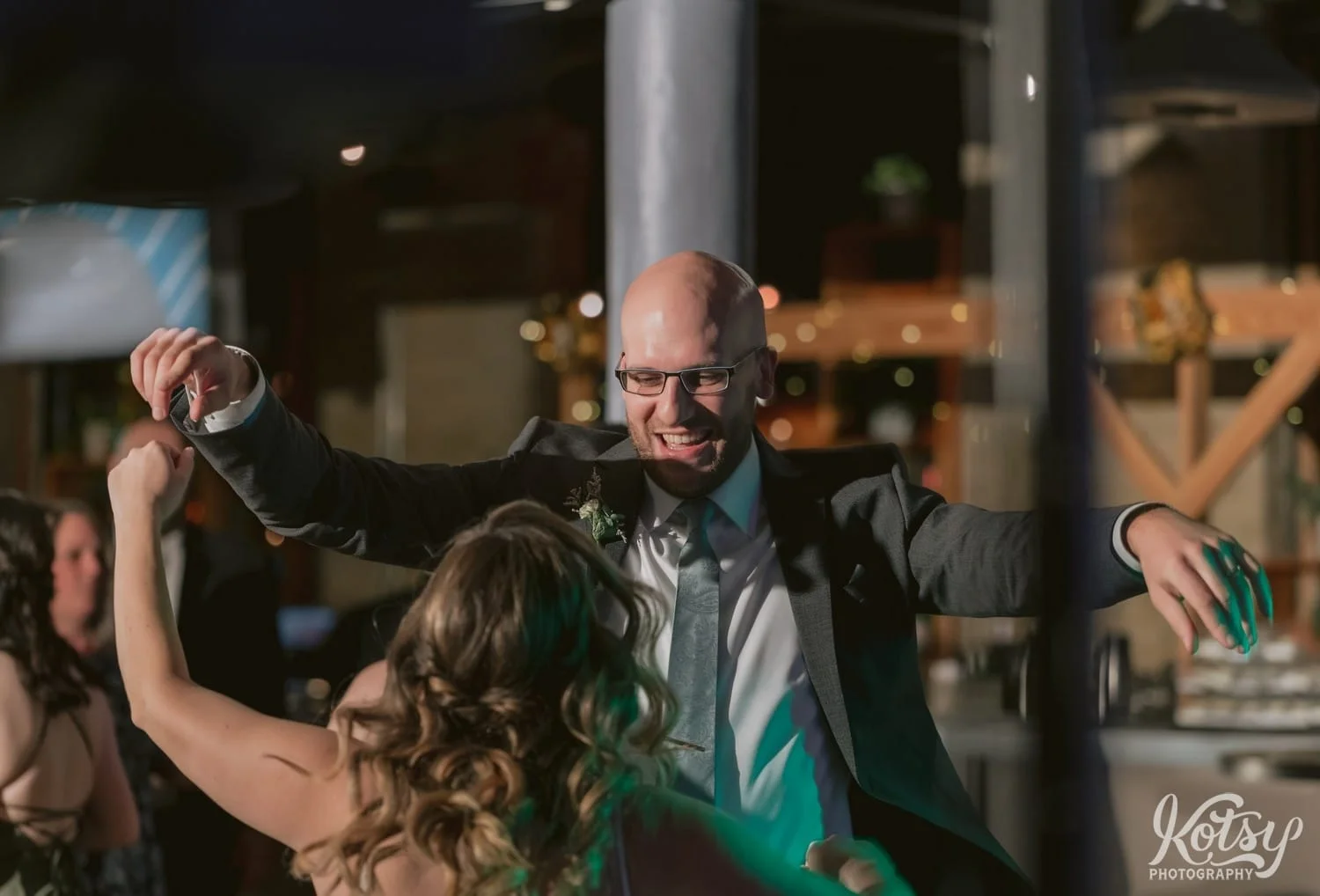 A groom and a gray suit and green tie is seen with his arms up dancing in front of his bride during their Second Floor Events wedding reception in Toronto, Canada.
