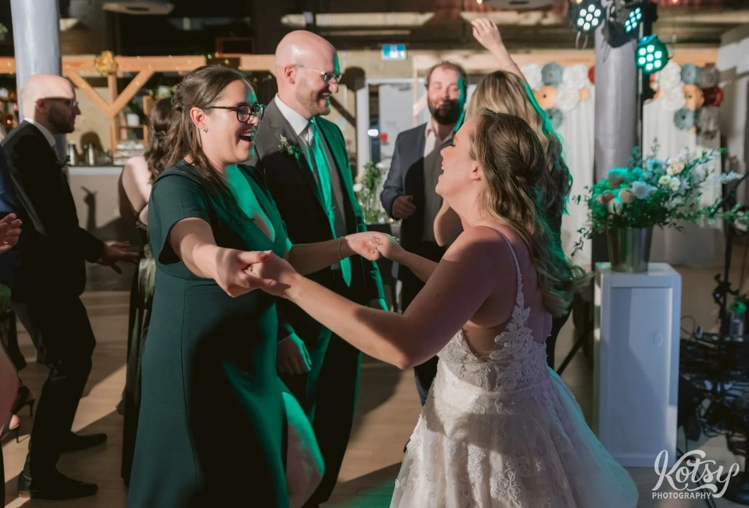 A woman in a green dress and a bride and a white wedding gown dance while holding hands during a Second Floor Events wedding reception in Toronto, Canada.