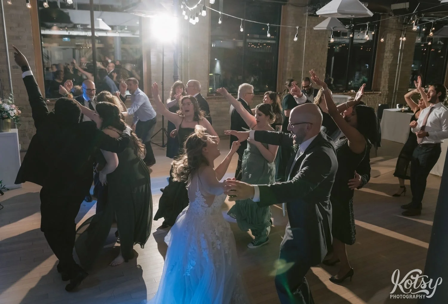 A large group of people dance with their hands in the air during a Second Floor Events wedding reception in Toronto, Canada.