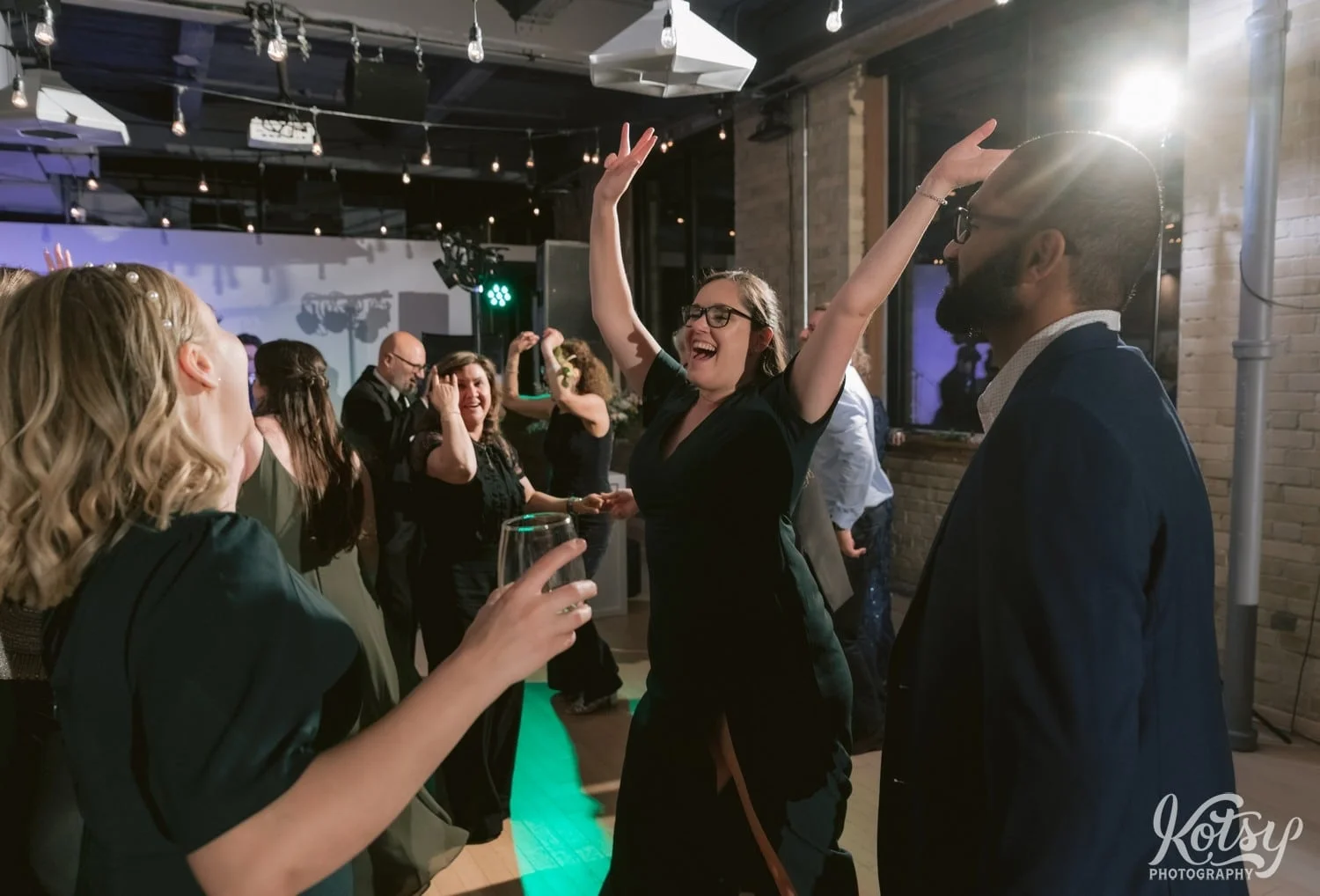 A woman in a green dress dances with her hands high in the air in a group of people during a Second Floor Events wedding reception in Toronto, Canada.