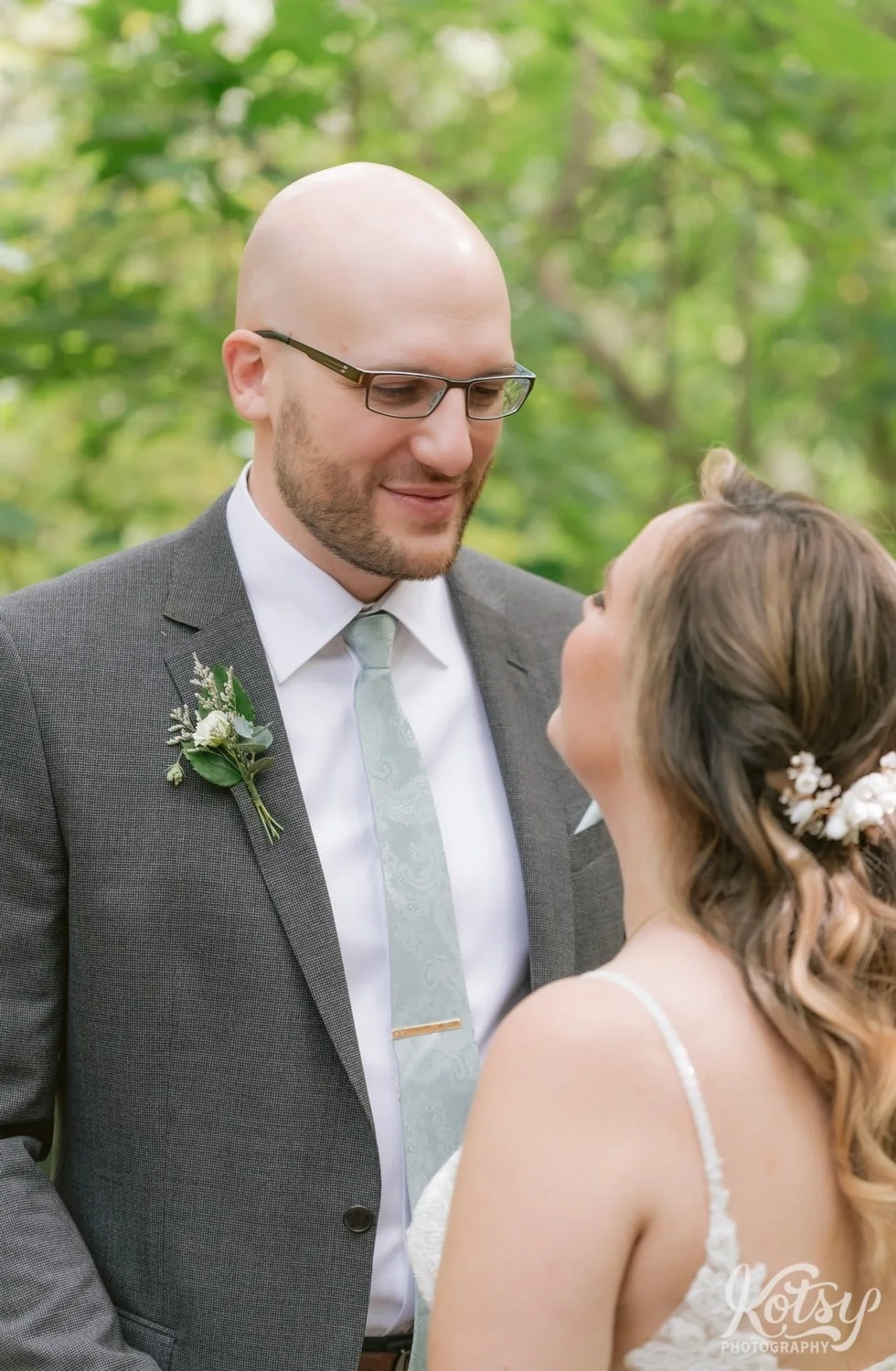 Closeup of a groom and a gray suit and green tie looking and smiling at his bride wearing a white bridle gown at West Deane Park in Toronto, Canada