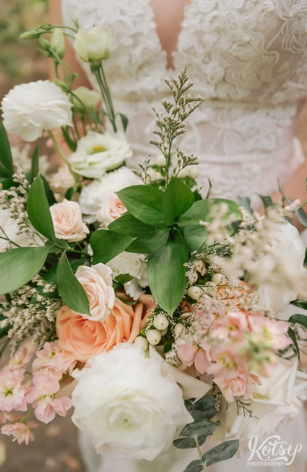 A close up shot of a flower bouquet held by a bride wearing a white bridal gown