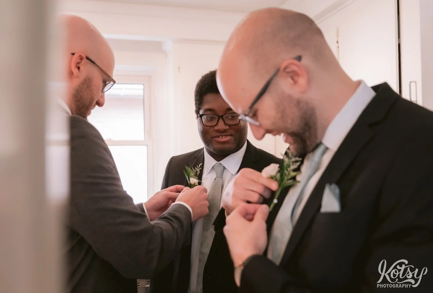 Three men getting ready for a wedding by adjusting their boutineers