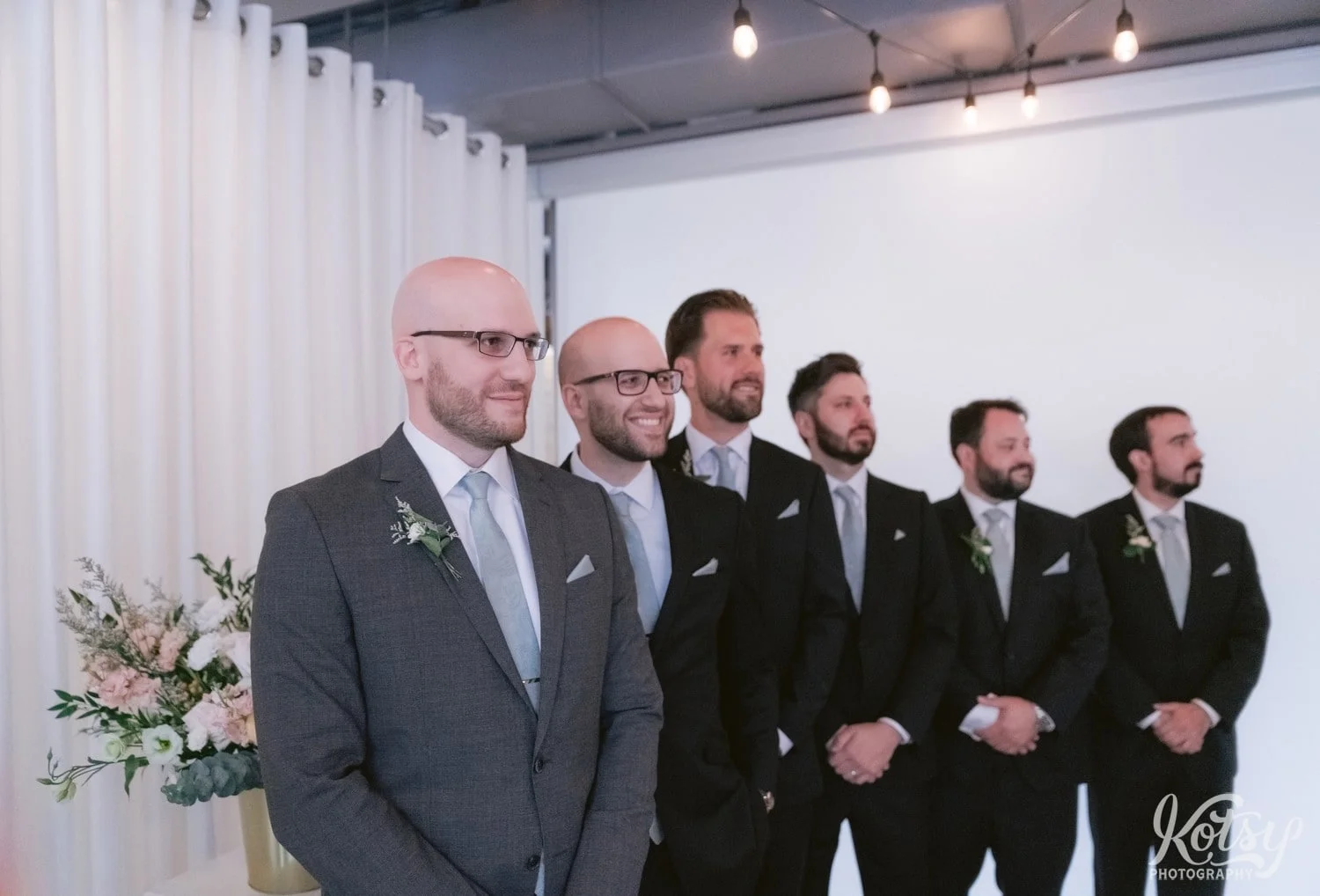A groom wearing a gray suit and green tie looks off camera smiling with groomsmen behind them during his Second floor events wedding ceremony in Toronto Canada