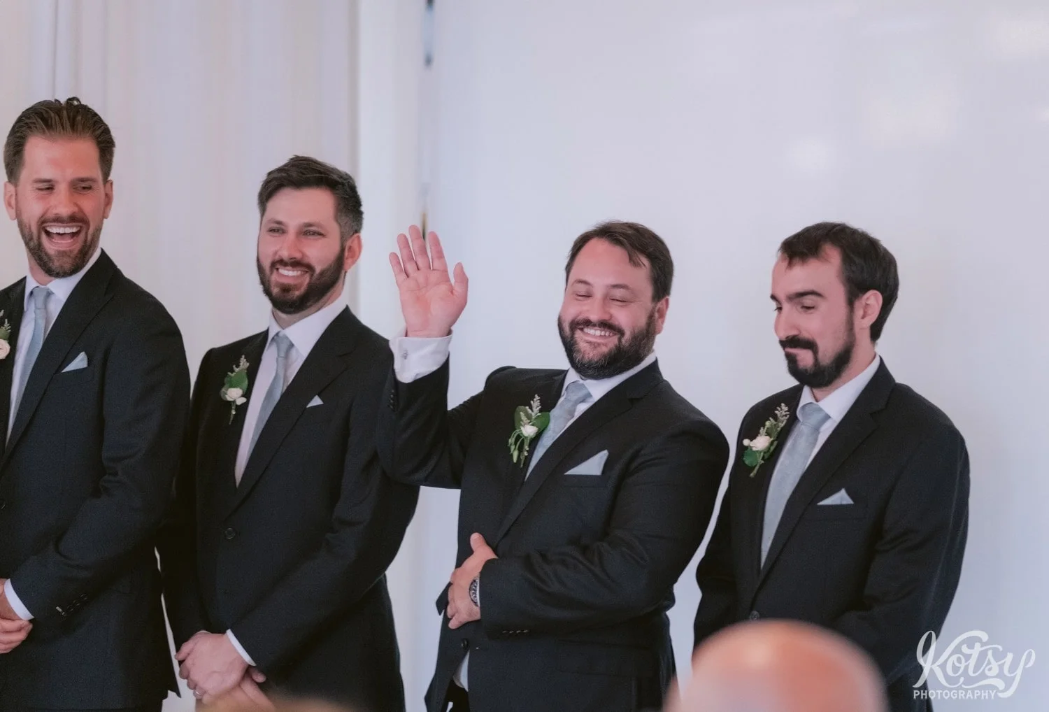 A groomsmen raises His hand and acknowledgement while he smiles during a Second Floor Events wedding ceremony in Toronto, Canada