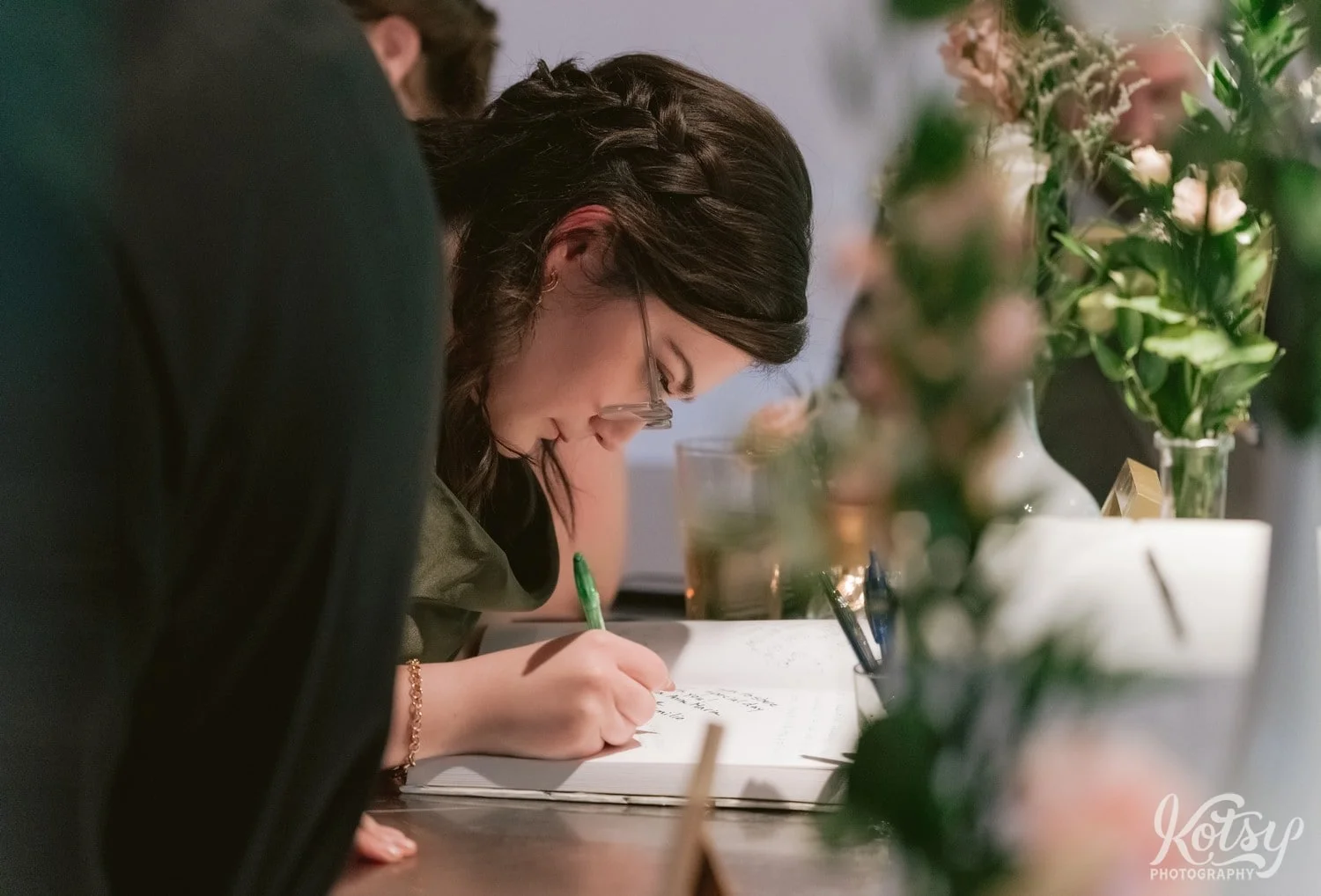 close up shot of a woman in a green dress writing in a guest book during a Second floor events wedding reception In Toronto Canada