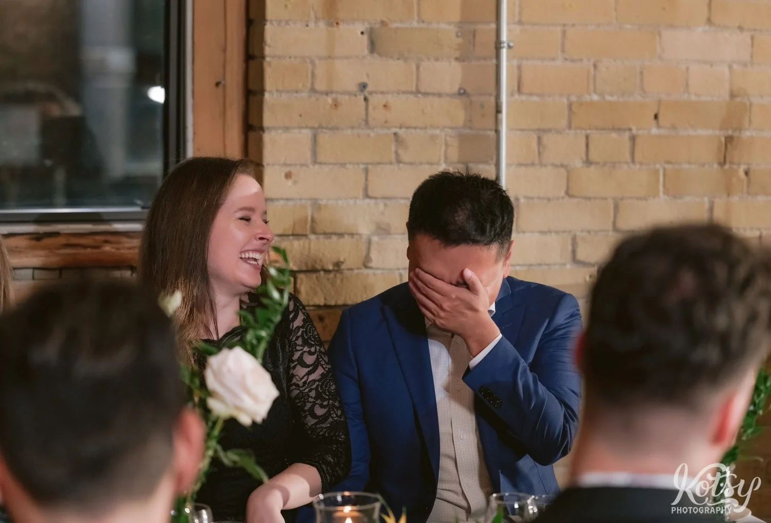 A man in a blue suit and a white dress shirt covers his face while laughing next to another woman laughing during a Second Floor Events wedding reception in Toronto, Canada.