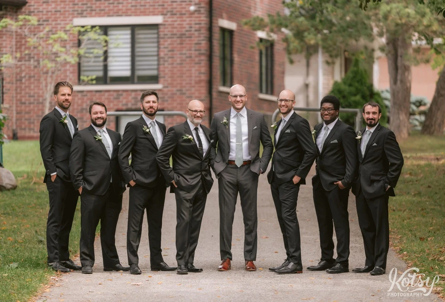 A shot of a groom and his seven groomsmen posing for a group shot on a pathway at West Deane Park in Toronto, Canada