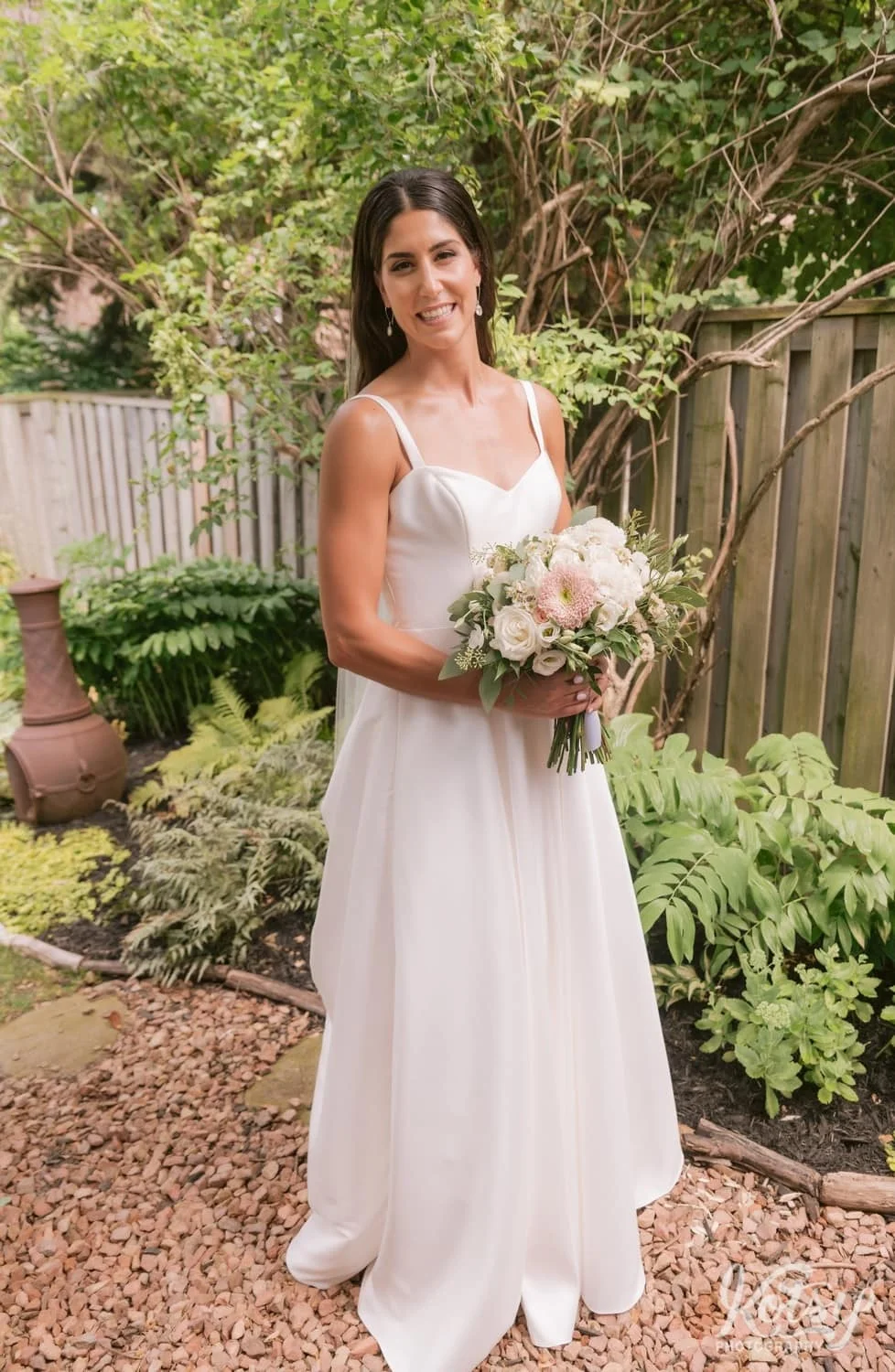 A bride poses for a solo portrait while wearing a white wedding gown and holding a bouquet of flowers.