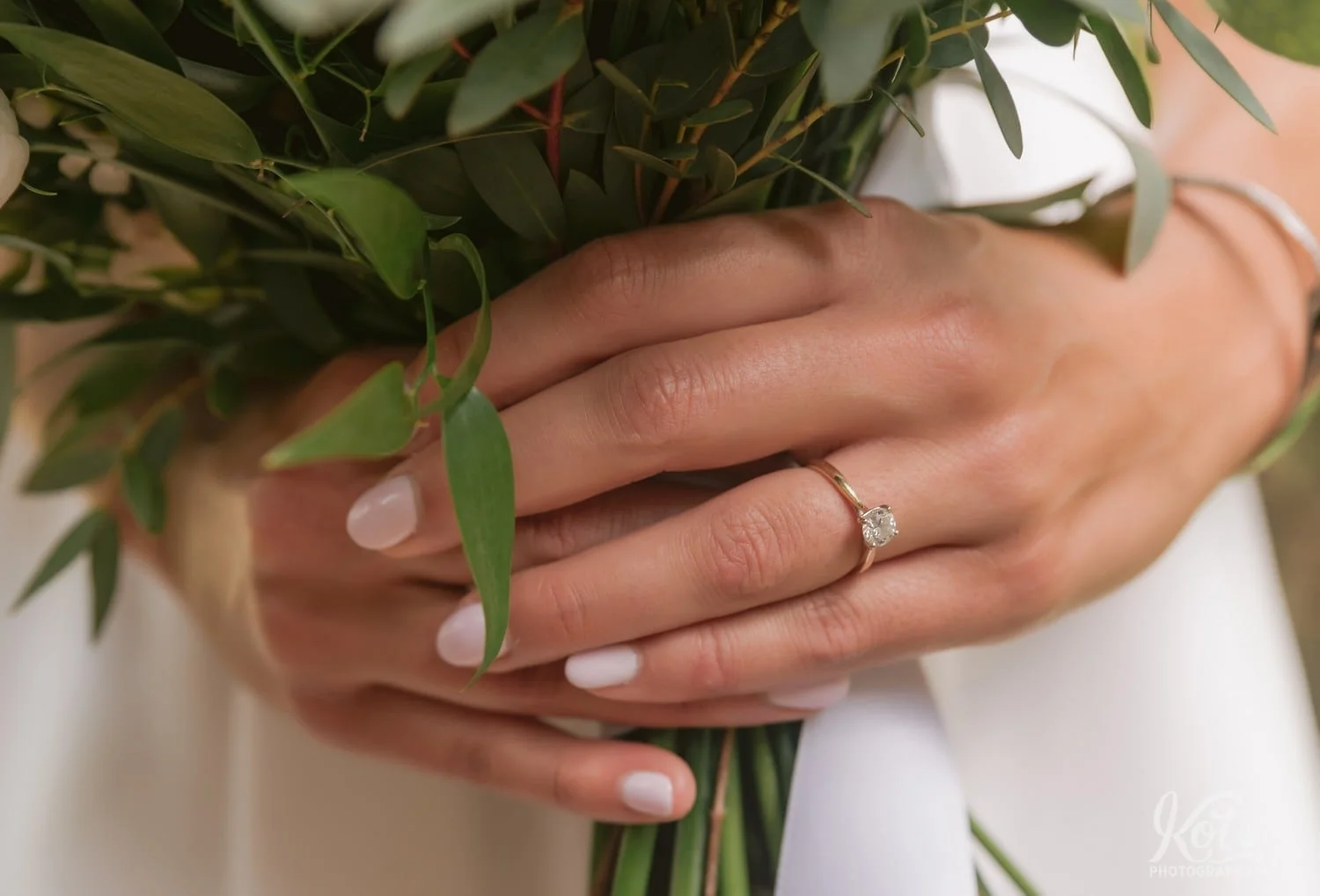 A close up of an engagement ring on a woman's hand holding a flower bouquet