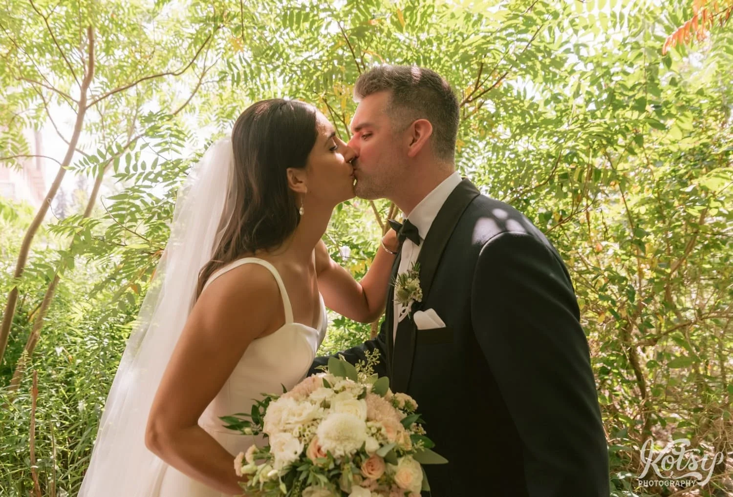A bride and groom kiss at the conclusion of their first look at Hunter's Point Wildlife Park in Toronto, Ontario, Canada