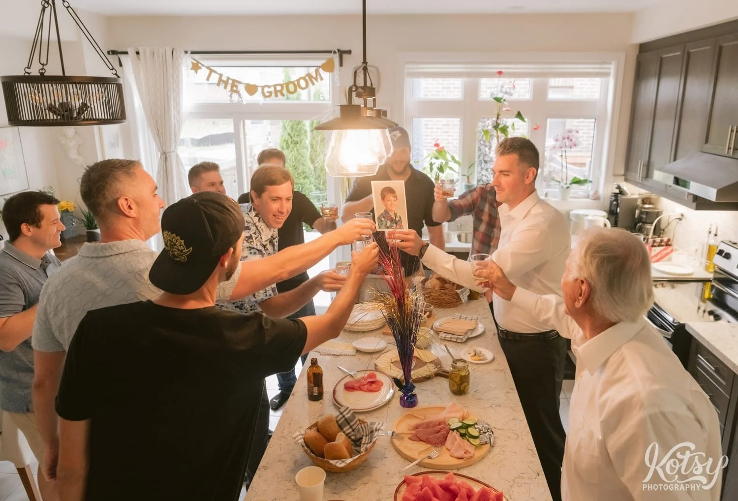 A large group of guys cheers a shot in a kitchen
