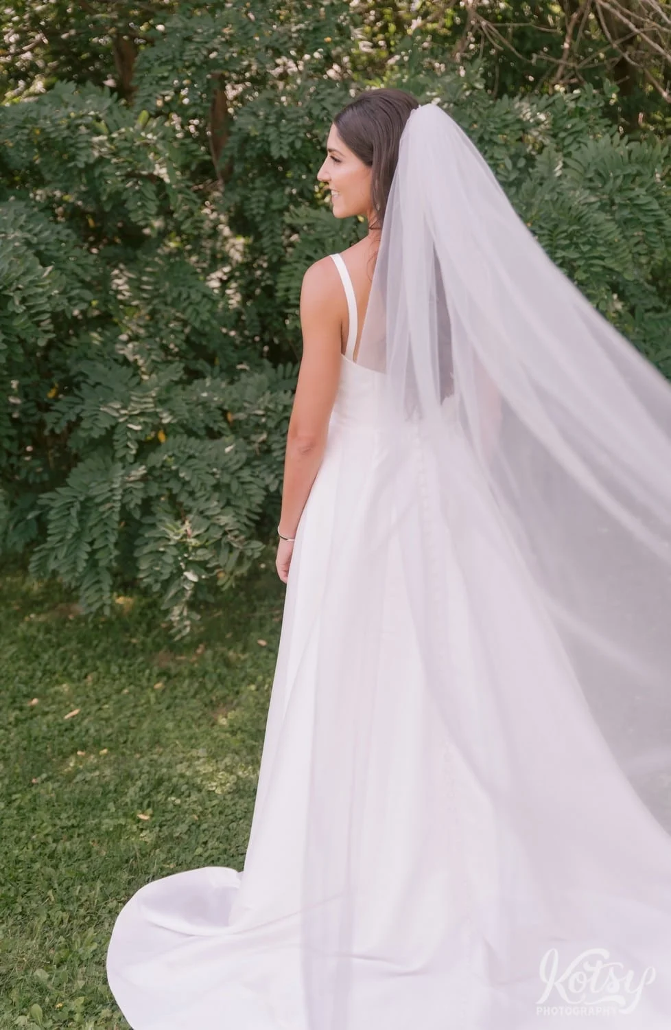 A bride's veil stretches from a groom's head to the camera as she stands at a park in Toronto, Canada