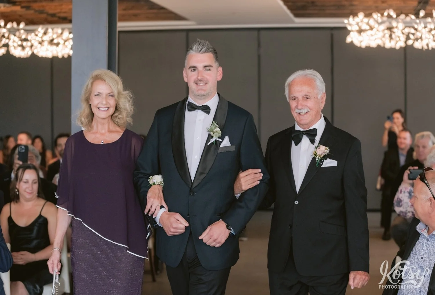 A groom walks down the aisle with his parents during his Village Loft wedding ceremony in Toronto, Canada