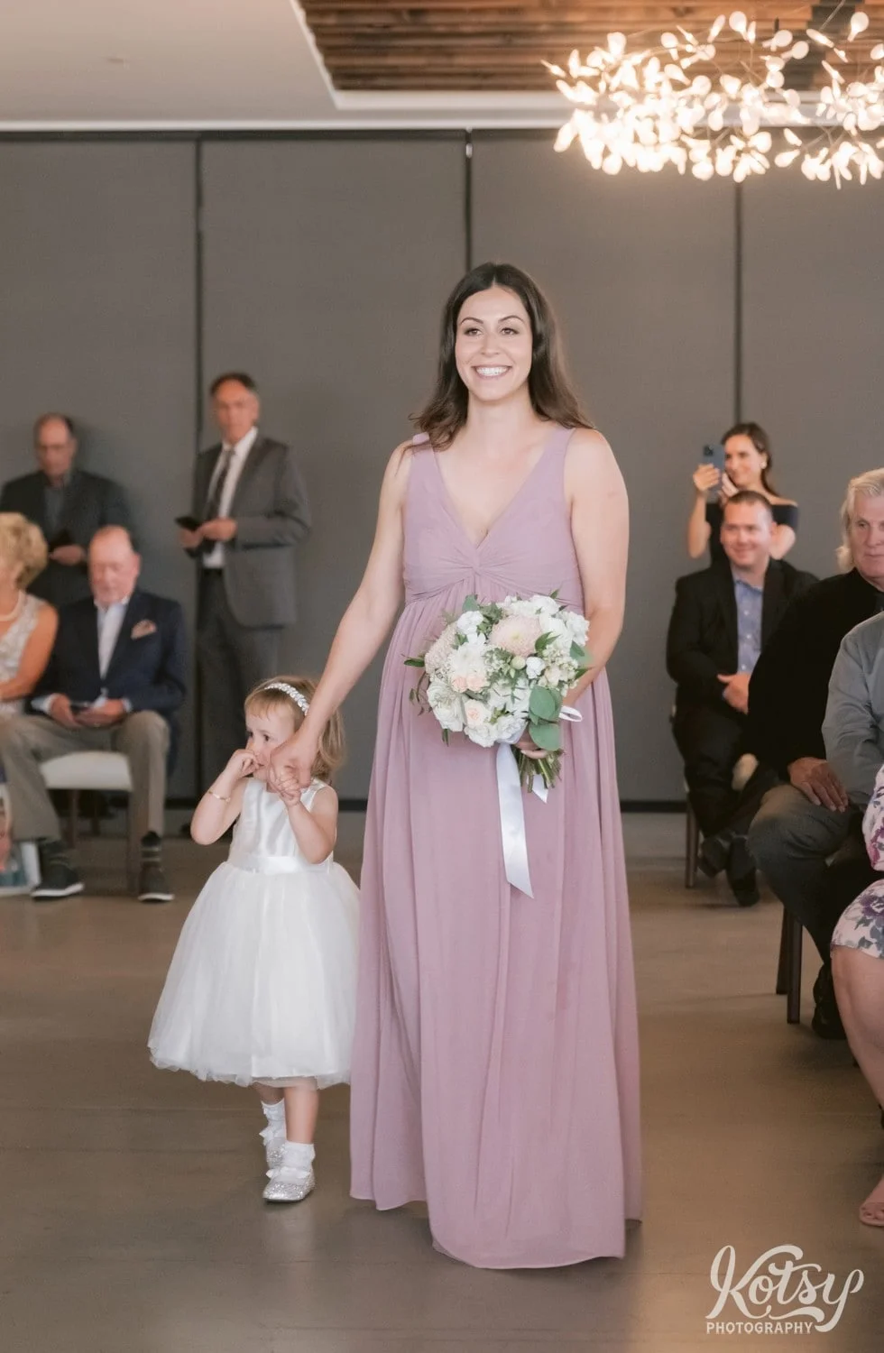 A woman in a pink dress walks down the aisle with a flower girl at a Village Loft wedding ceremony in Toronto, Canada