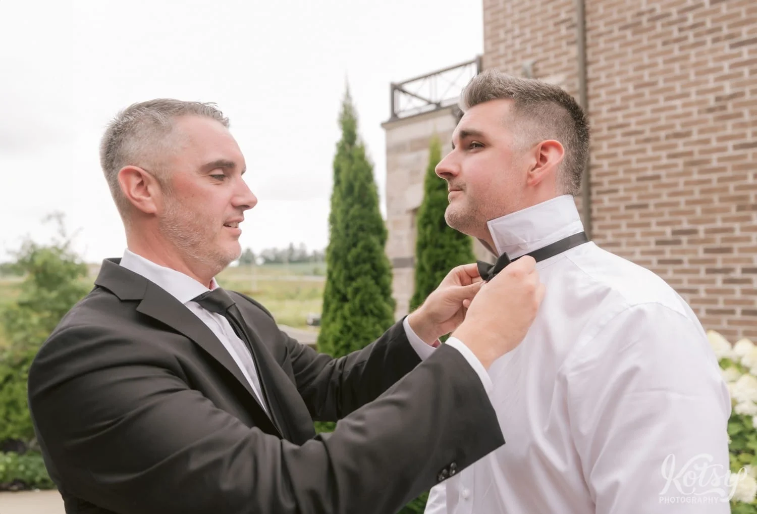 A man in a black suit adjusts his brothers bow-tie