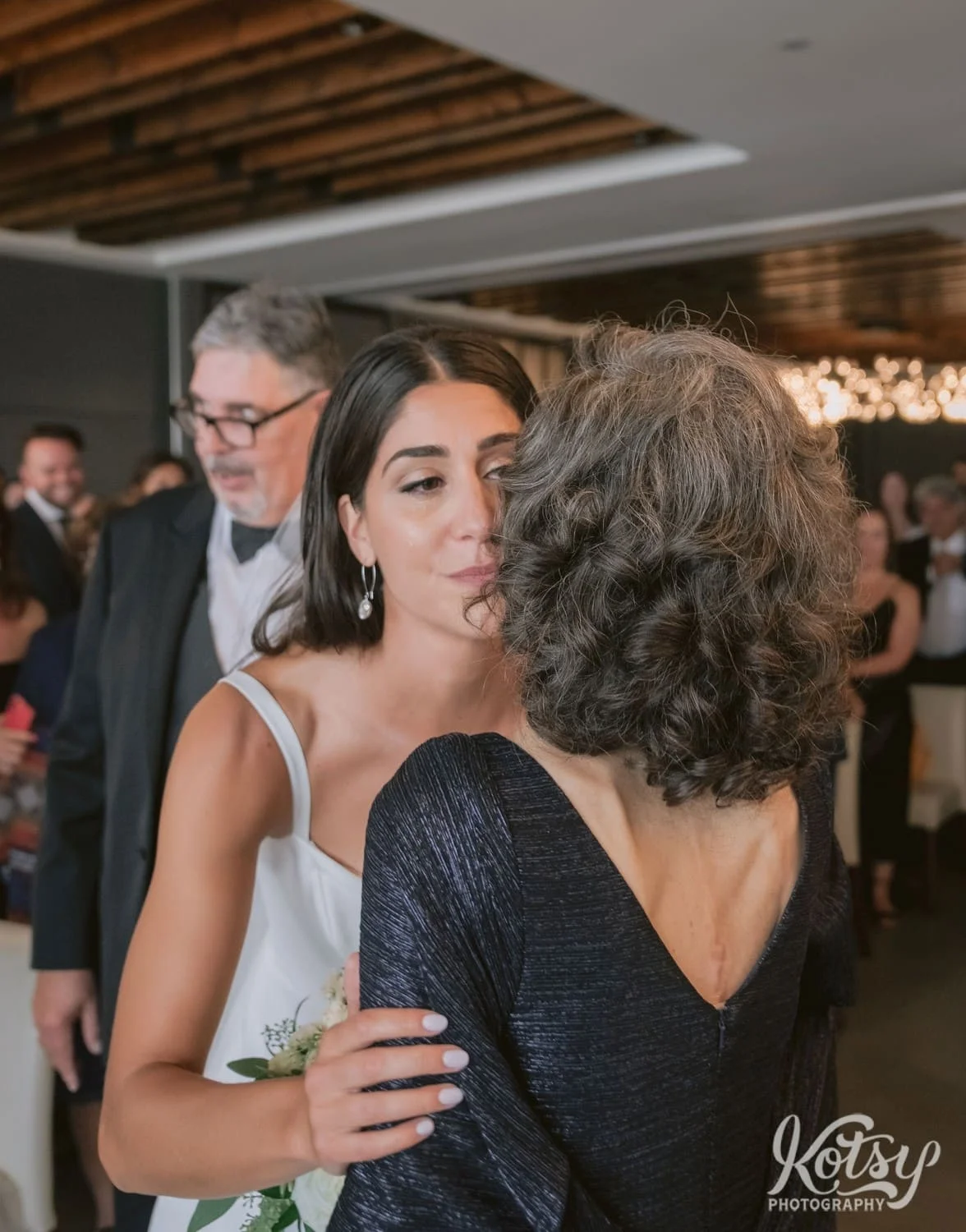 A bride kisses her mother on the cheek at the end of the aisle during a Village Loft wedding ceremony in Toronto, Canada