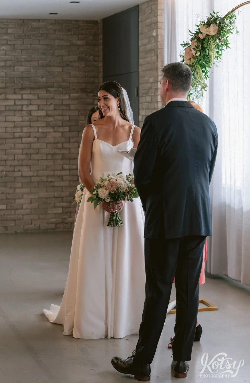 A bride smiles at guests off camera during a Village Loft wedding ceremony in Toronto, Canada