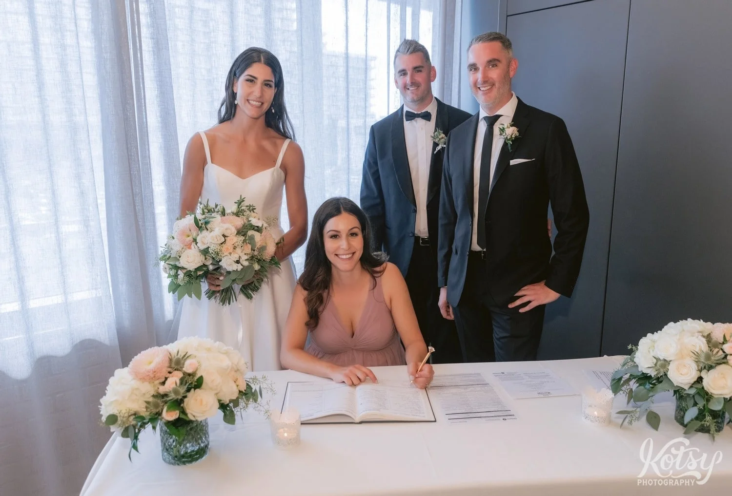 A bride, groom and their brother and sister pose for a group photo during the witness signing at a Village Loft wedding ceremony in Toronto, Canada