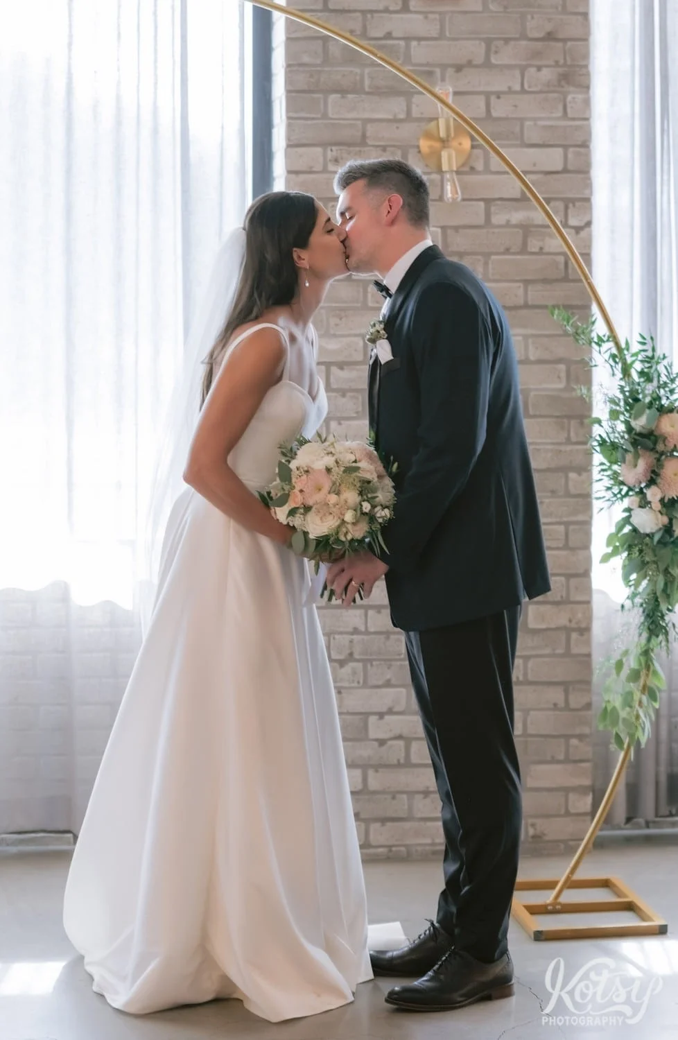 A full body shot of a bride and groom enjoying their first kiss during a Village Loft wedding ceremony in Toronto, Canada