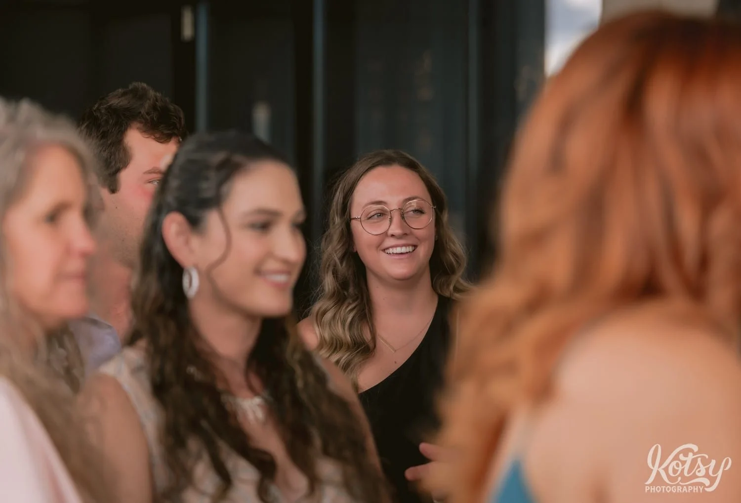 A smiling woman is seen through a group of people during cocktail hour at a Village Loft wedding reception in Toronto, Canada