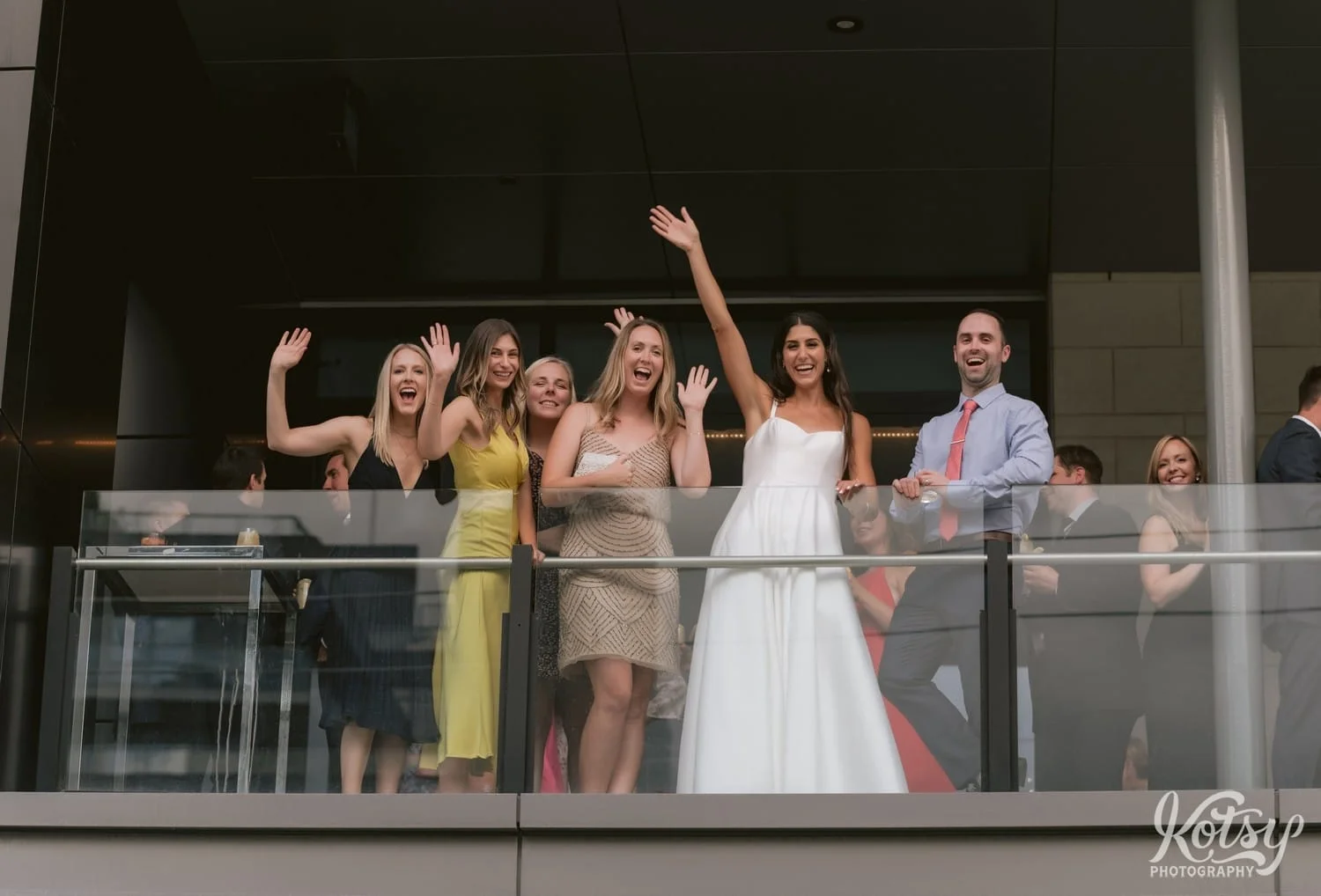 A bride and group of guests wave to the camera from a balcony during a Village Loft wedding reception in Toronto, Canada