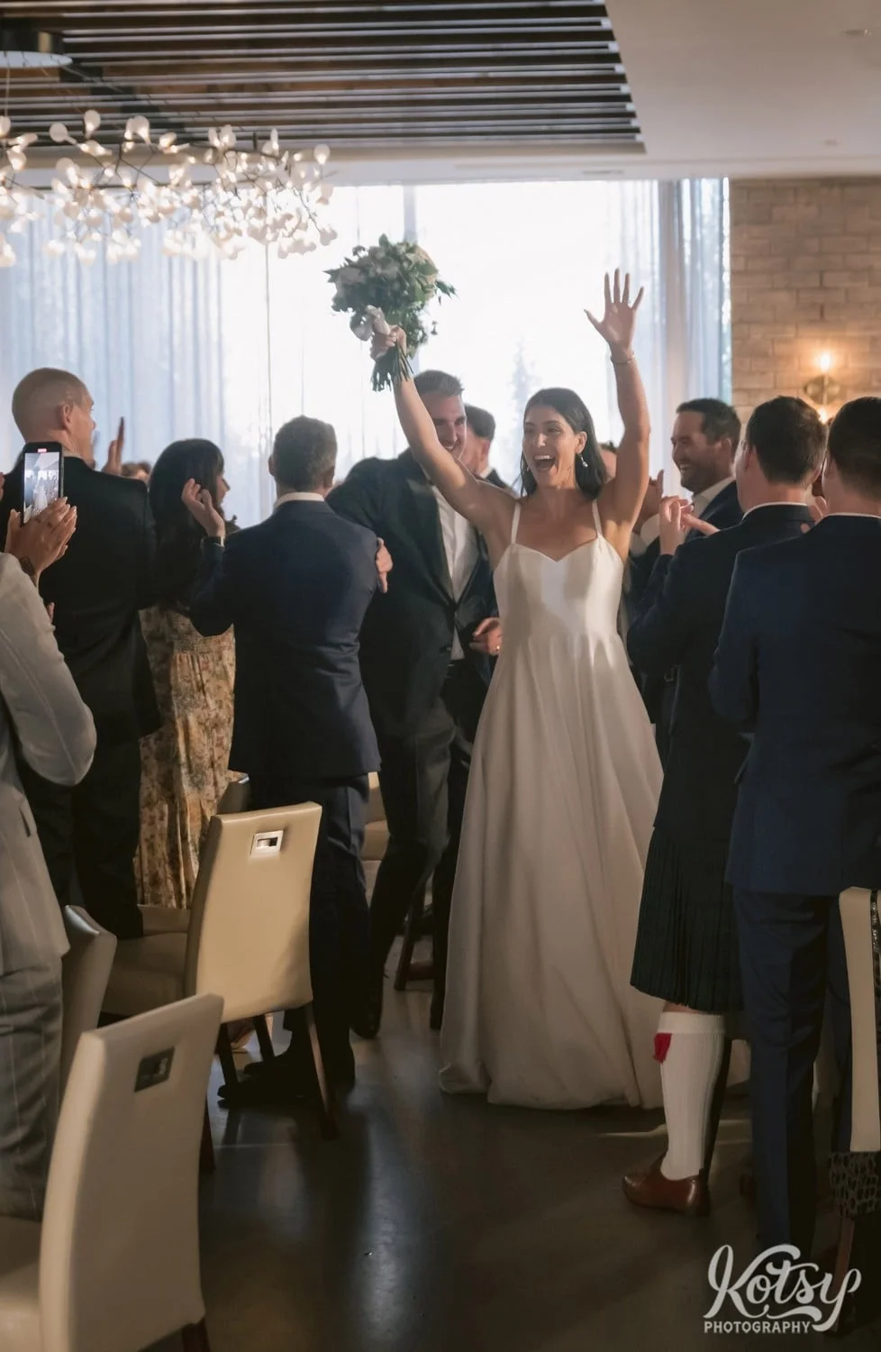 A bride has her hands up in the air as she and her groom make their entrance during their Village Loft wedding reception in Toronto, Canada