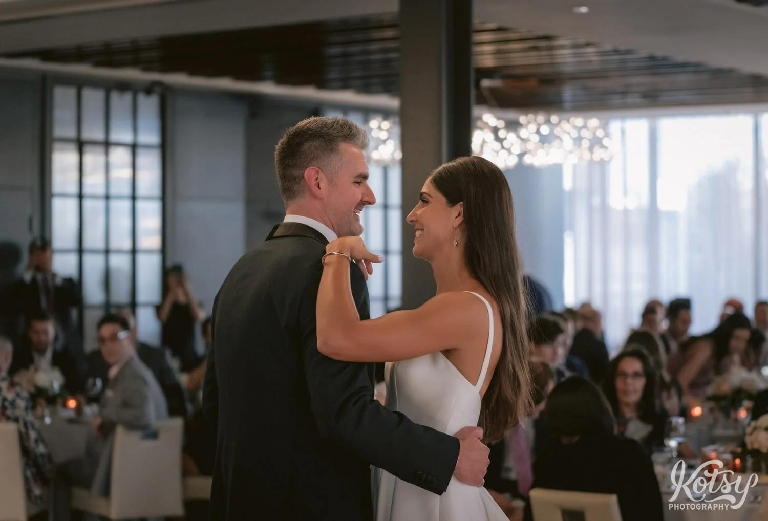A bride and groom smile at each other while they enjoy a first dance during their Village Loft wedding reception in Toronto, Canada