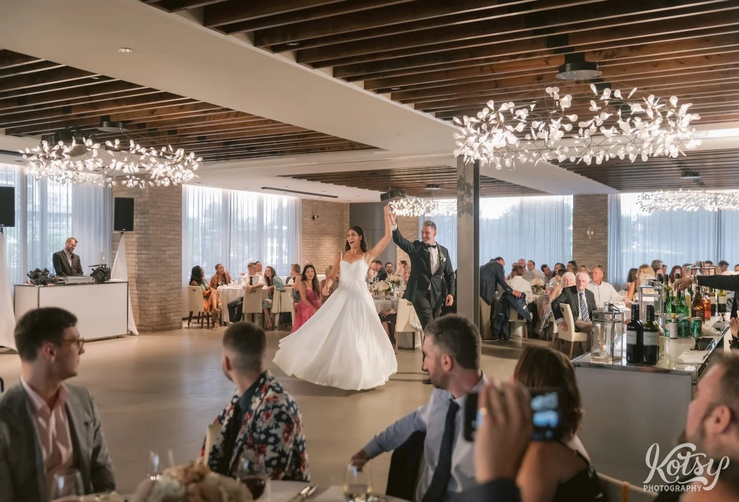 A bride and groom raise their hands in front of all their guests during their Village Loft wedding reception in Toronto, Canada