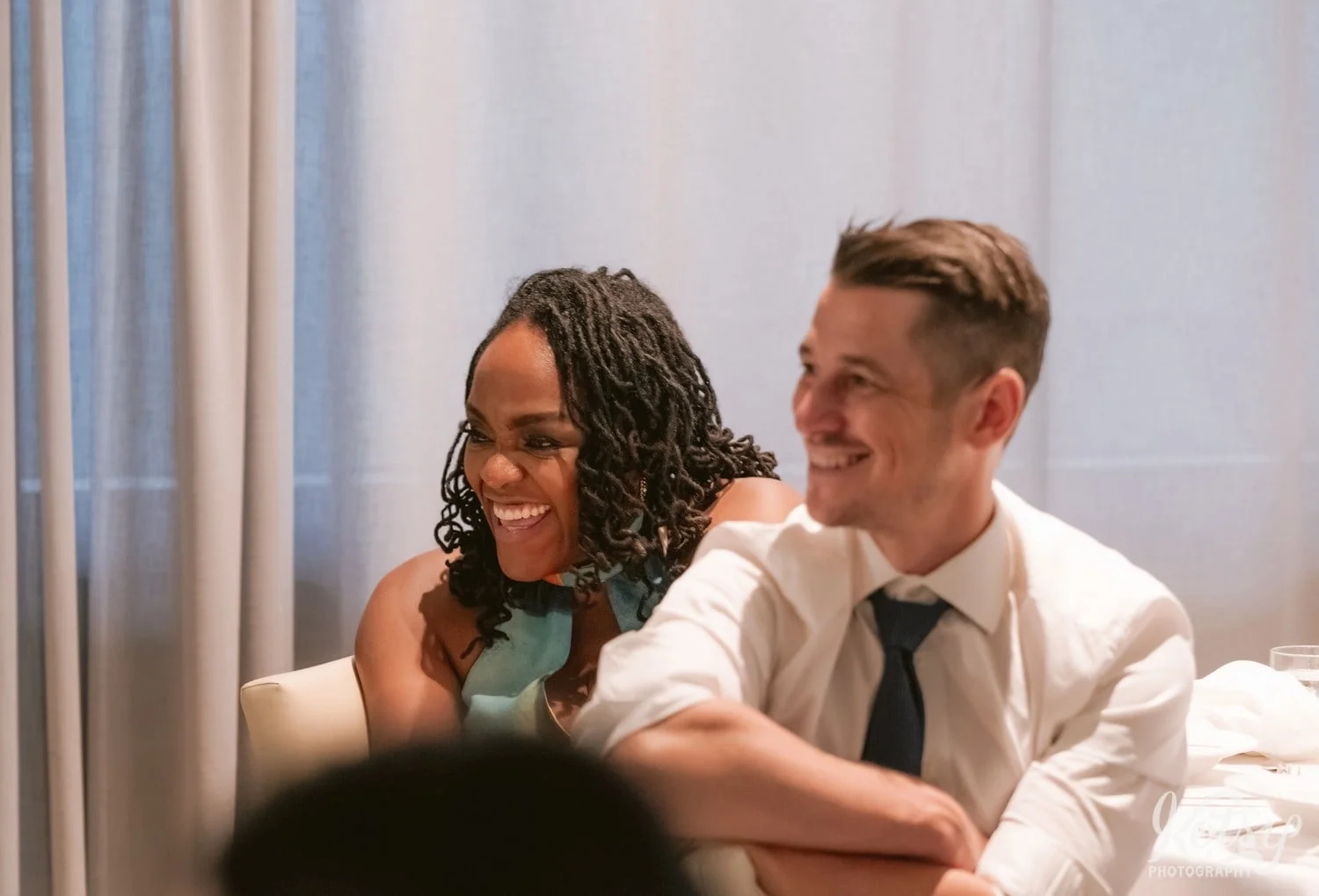 A woman and man enjoy a laugh while sitting at a table during a Village Loft wedding reception in Toronto, Canada