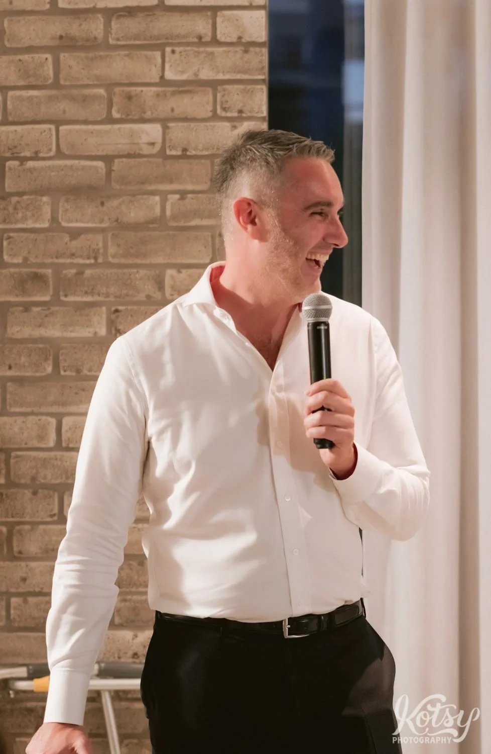 A man smiles big as he makes a speech during a Village Loft wedding reception in Toronto, Canada