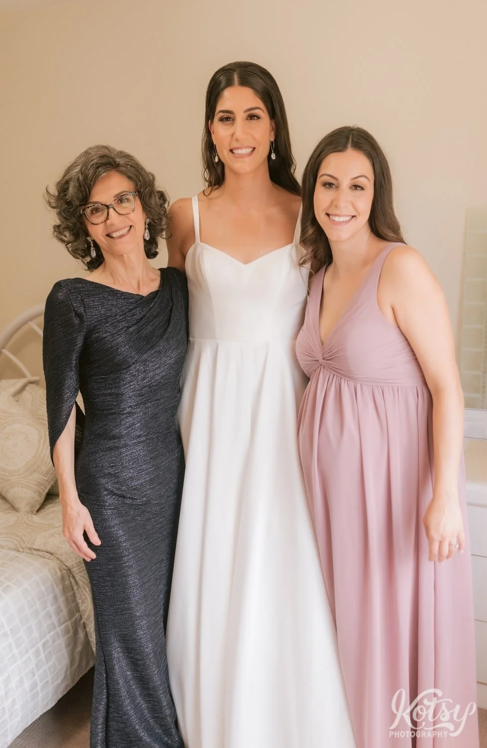 A bride wearing a white wedding gown poses for a group photo with her mother and sister.