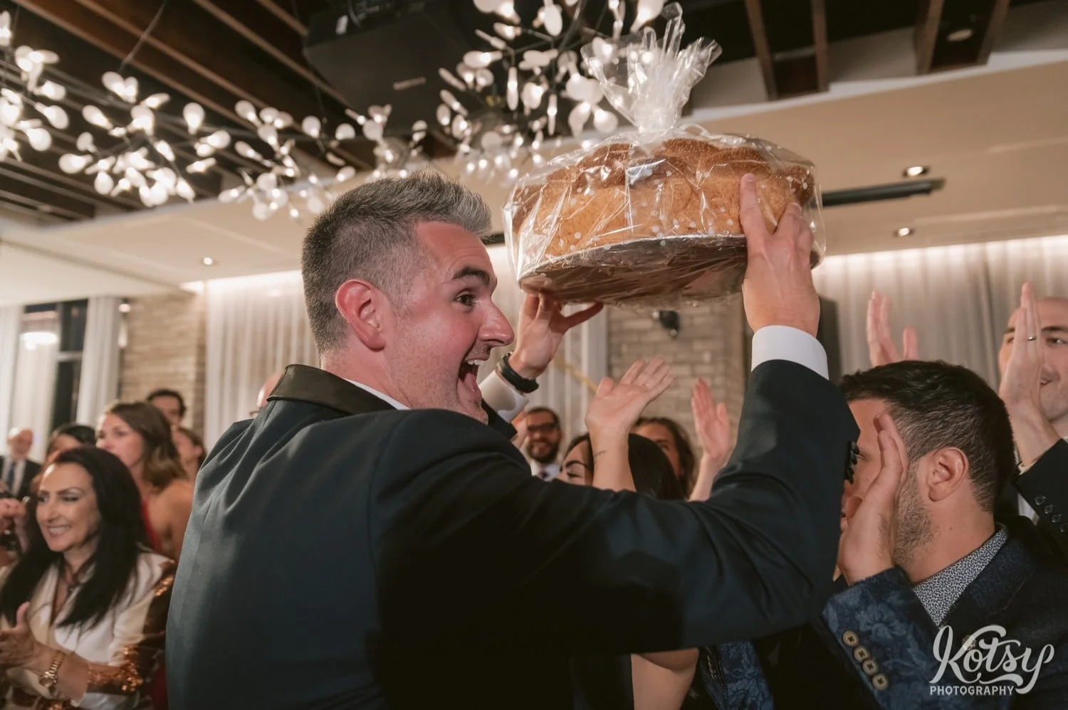 A groom smiles big as he hold a big loaf of bread at his Village Loft wedding reception in Toronto, Canada