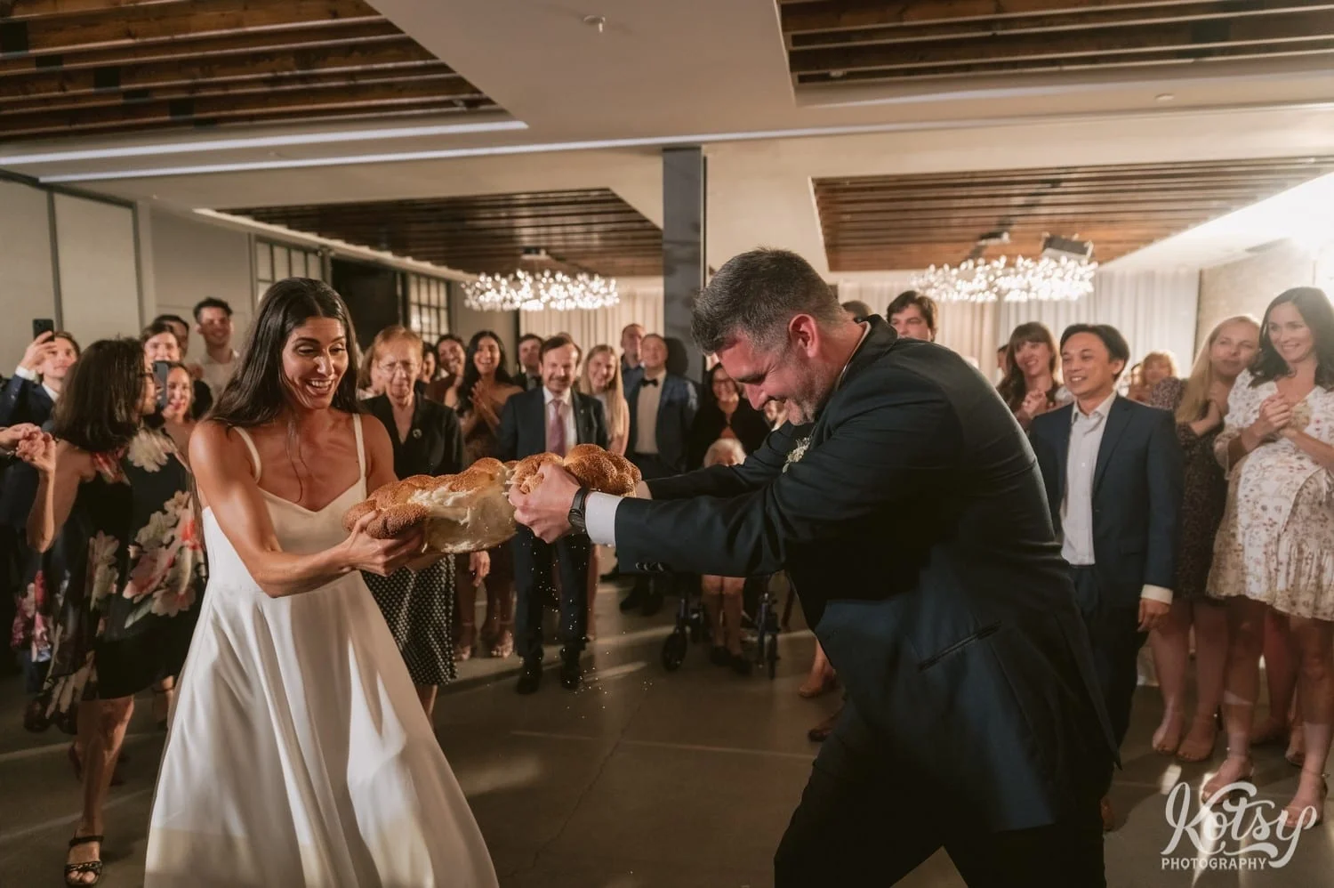 A bride and groom tug on a large loaf of bread during the Macedonian breaking of the bread ceremony during a Village Loft wedding reception in Toronto, Canada