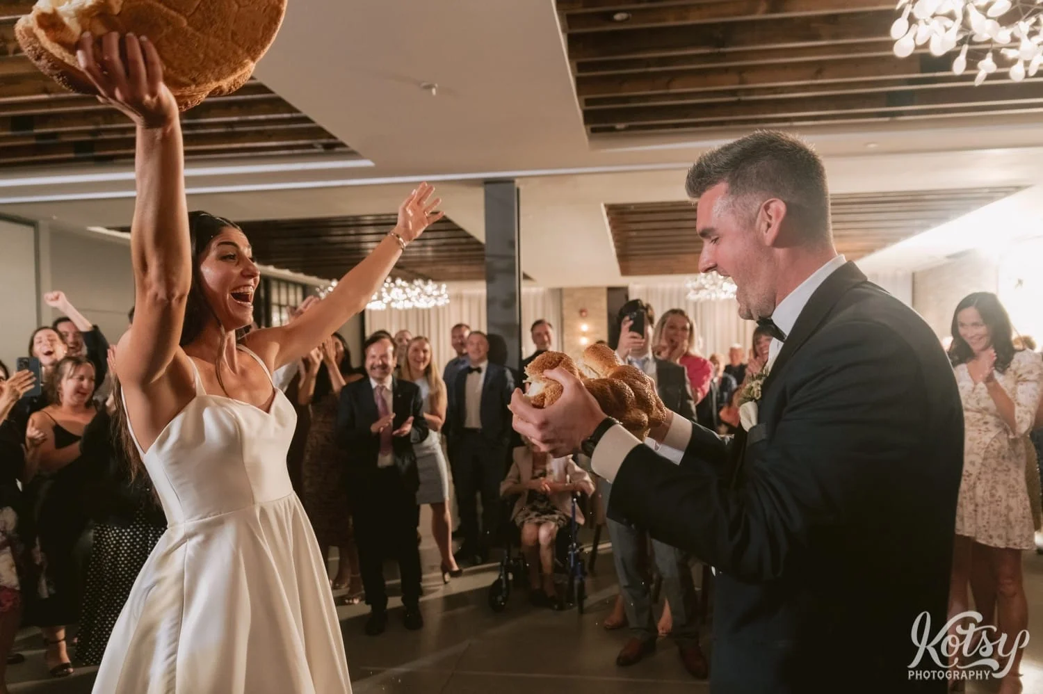 A bride holds up her larger half after a Macedonian breaking of the bread ceremony at Village Loft wedding reception in Toronto, Canada
