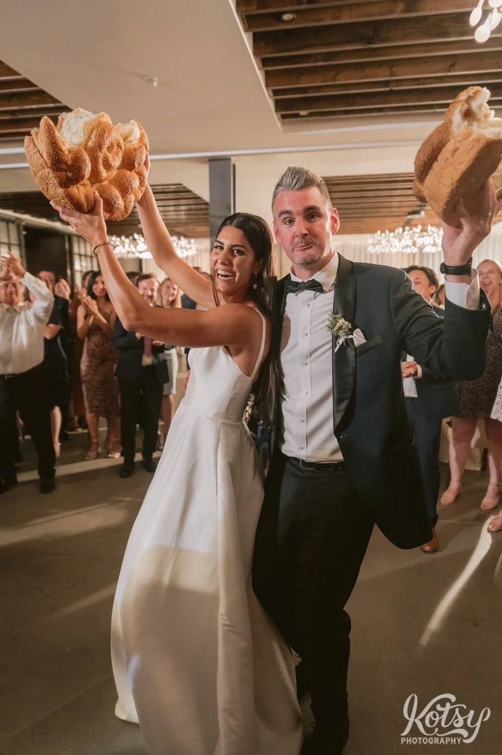 A bride and groom hold up their respective halves of bread after the Macedonian breaking of the bread ceremony at their Village Loft wedding reception in Toronto, Canada