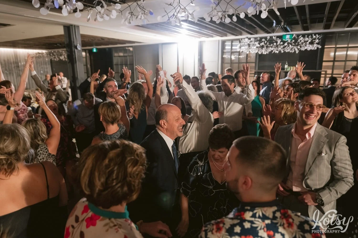A room full of people raise their hands while dancing at a Village Loft wedding reception in Toronto, Canada