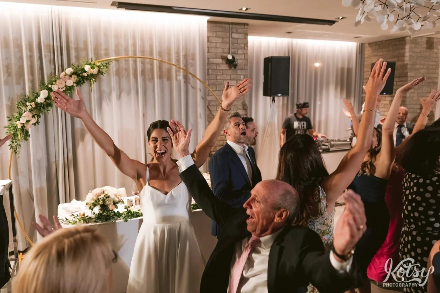Hands are in the air as a bride and other wedding guests do the YMCA at a Village Loft wedding reception in Toronto, Canada