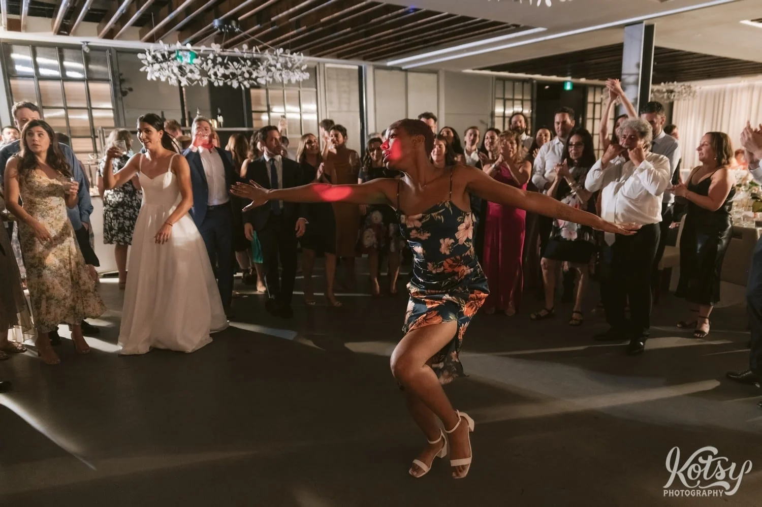 A woman dances with her arms wide out in front of a group of guests during a Village Loft wedding reception in Toronto, Canada