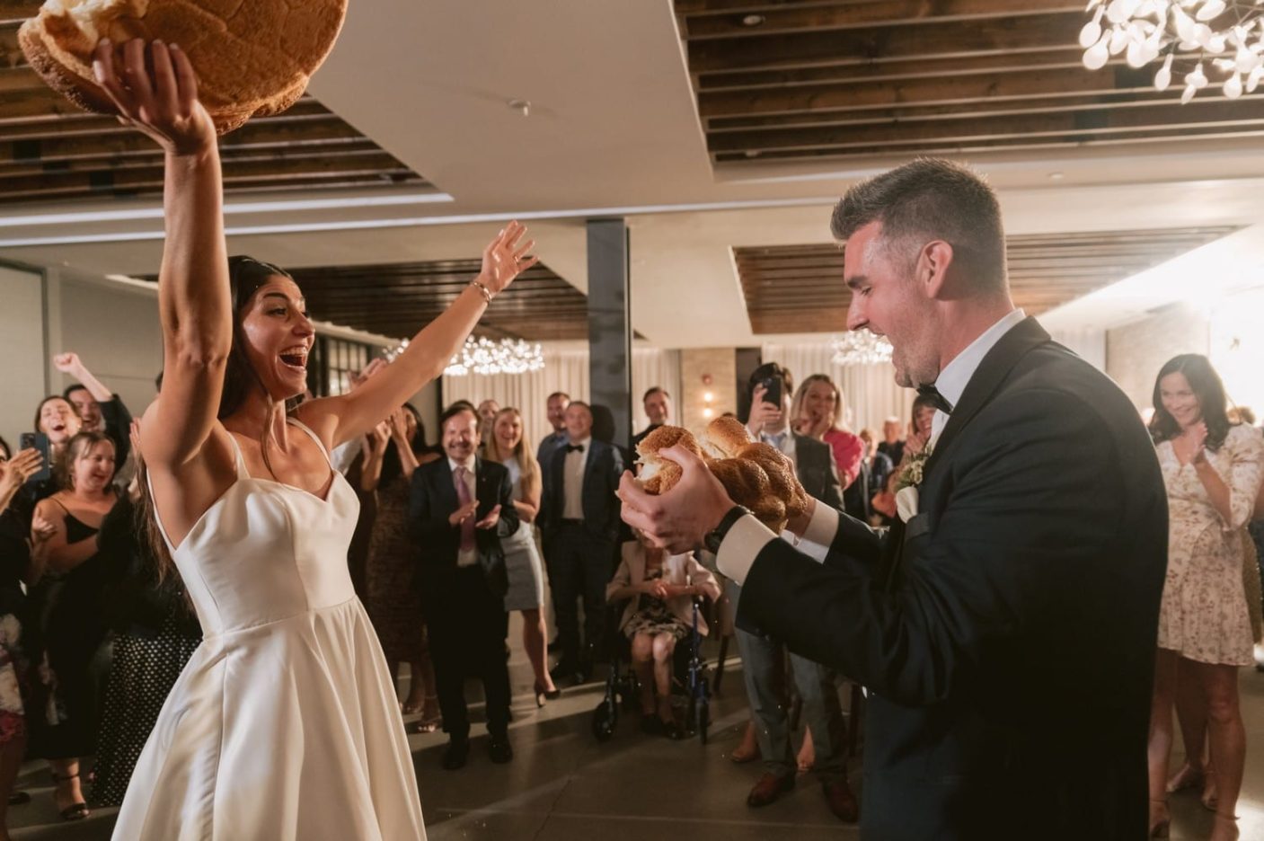 A bride holds a bi chunk of bread in the air after winning the breaking of the bread ceremony at her Village Loft Wedding in Toronto