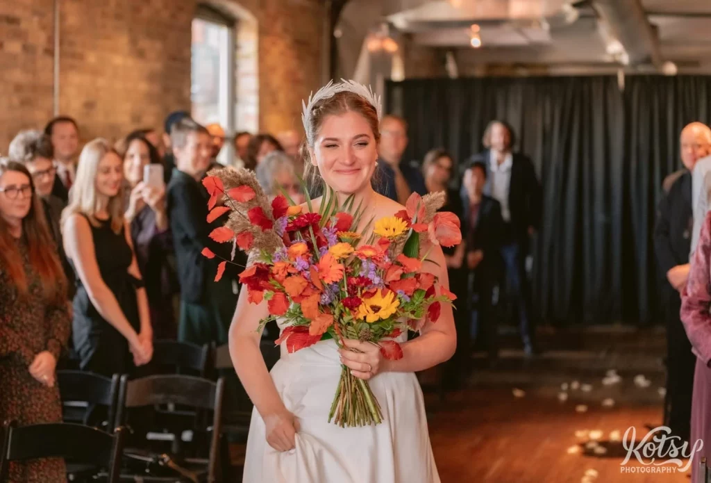 A bride carrying a large flower bouquet makes an entrance during her Burroughes Building wedding ceremony in Toronto, Canada