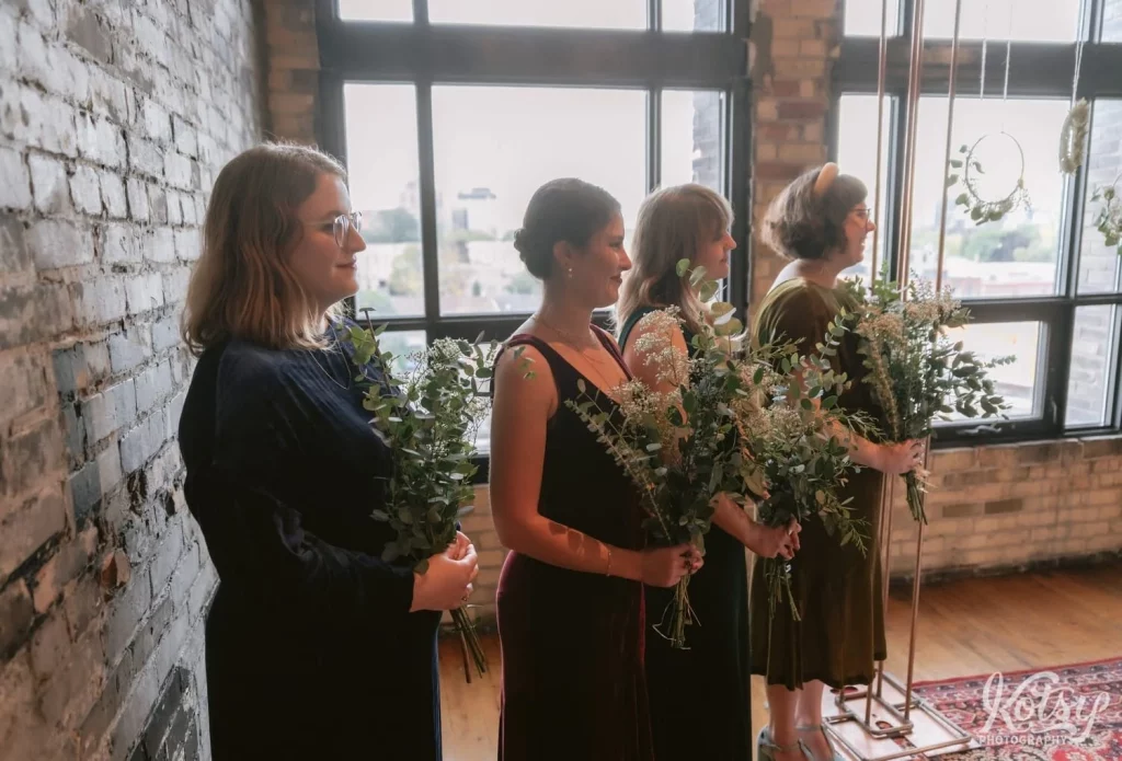 Four bridesmaids stand with eucalyptus and babies breath in their hands as they watch their friend during her Burroughes Building wedding ceremony in Toronto, Canada