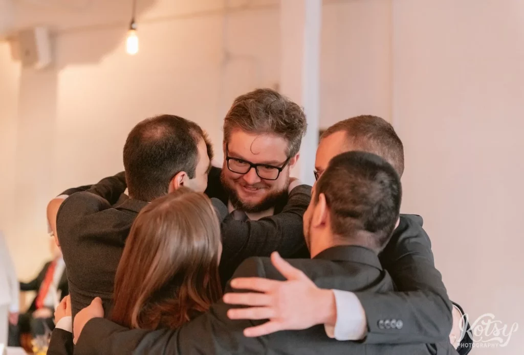 A groom hugs a group of people at the conclusion of his Burroughes Building wedding ceremony in Toronto, Canada